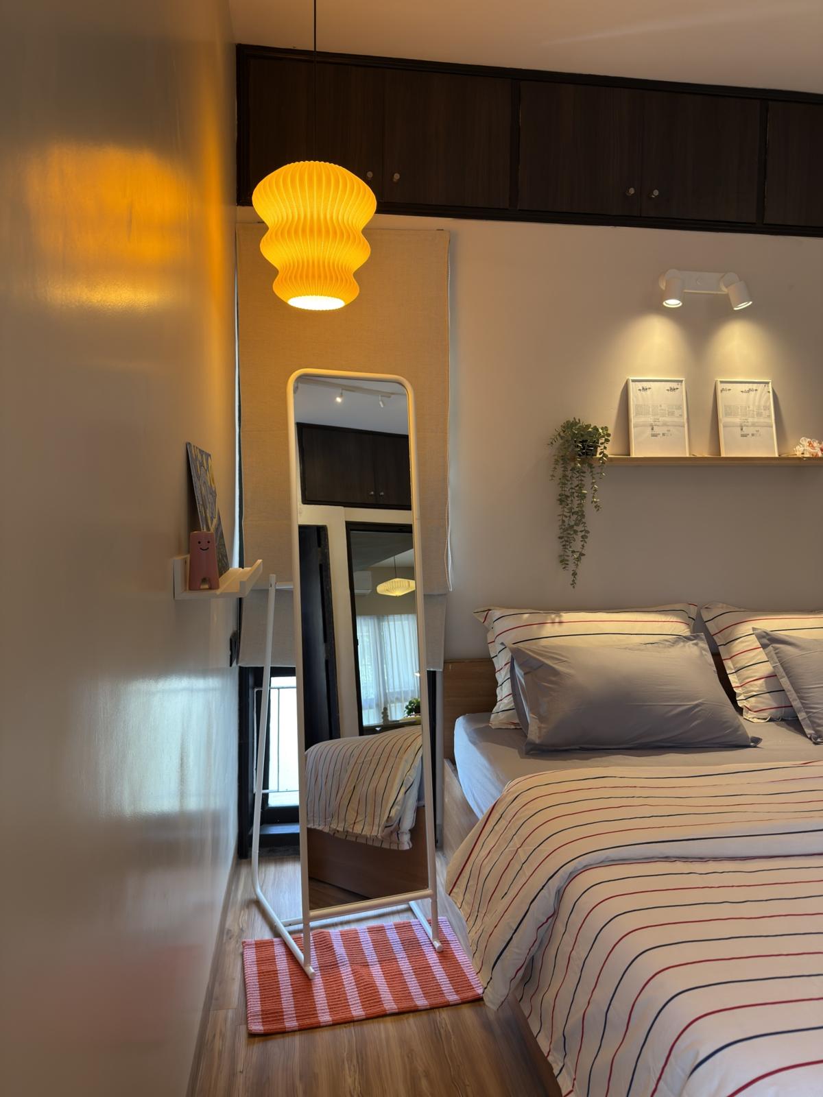 A glowing amber pleated pendant lamp beside a striped bed